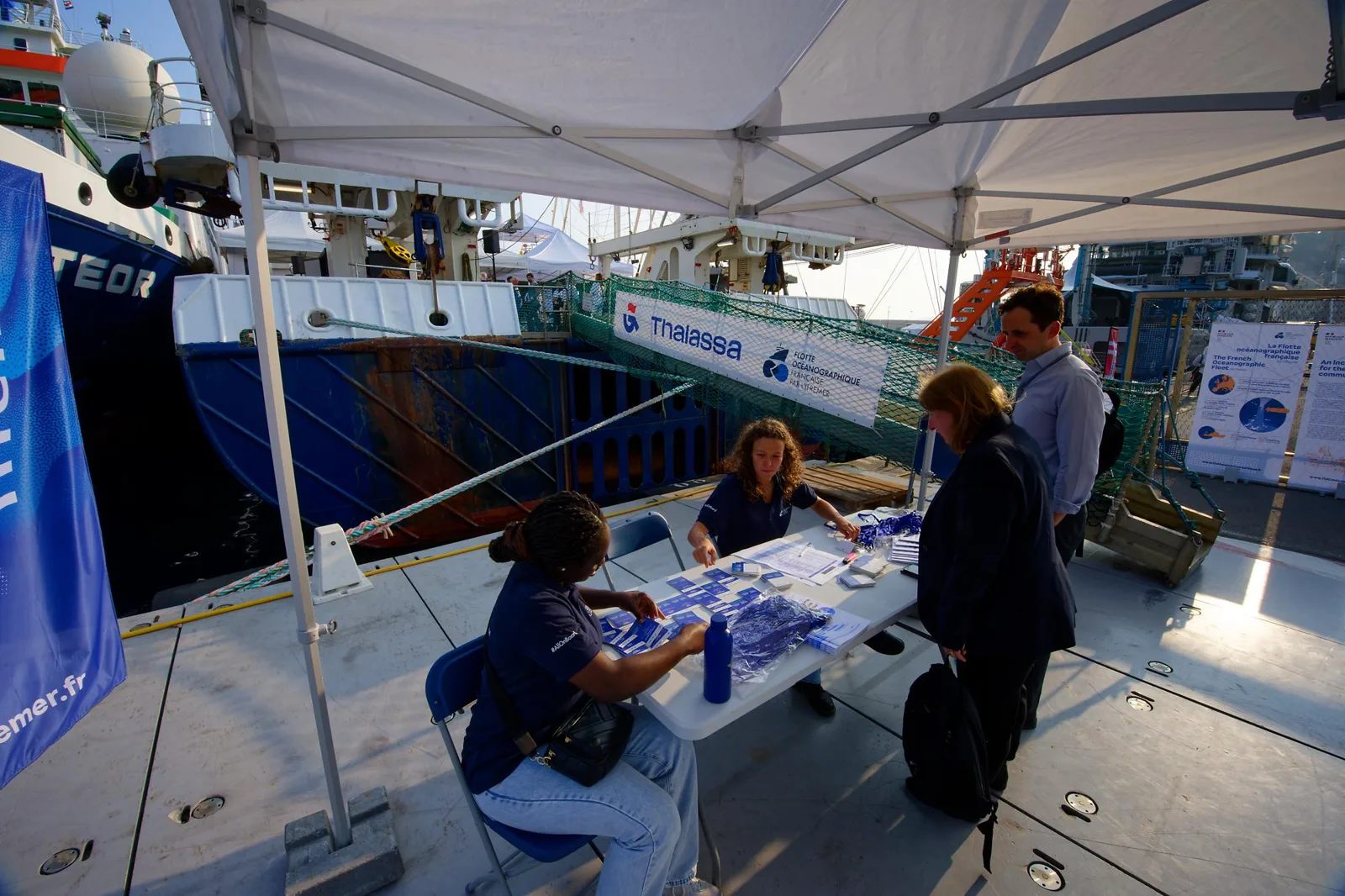 Visitors checking in at a welcome desk beside a research vessel.