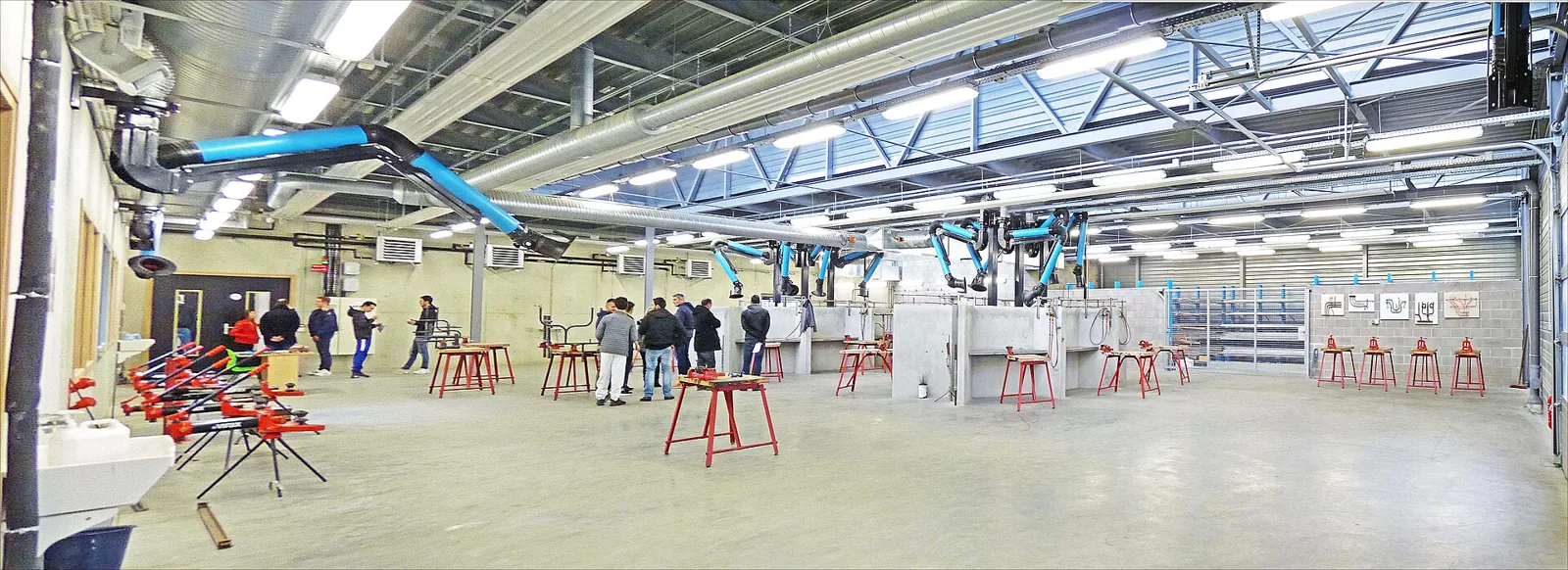 Rows of plumbing training stations and pipework inside a spacious apprenticeship workshop.