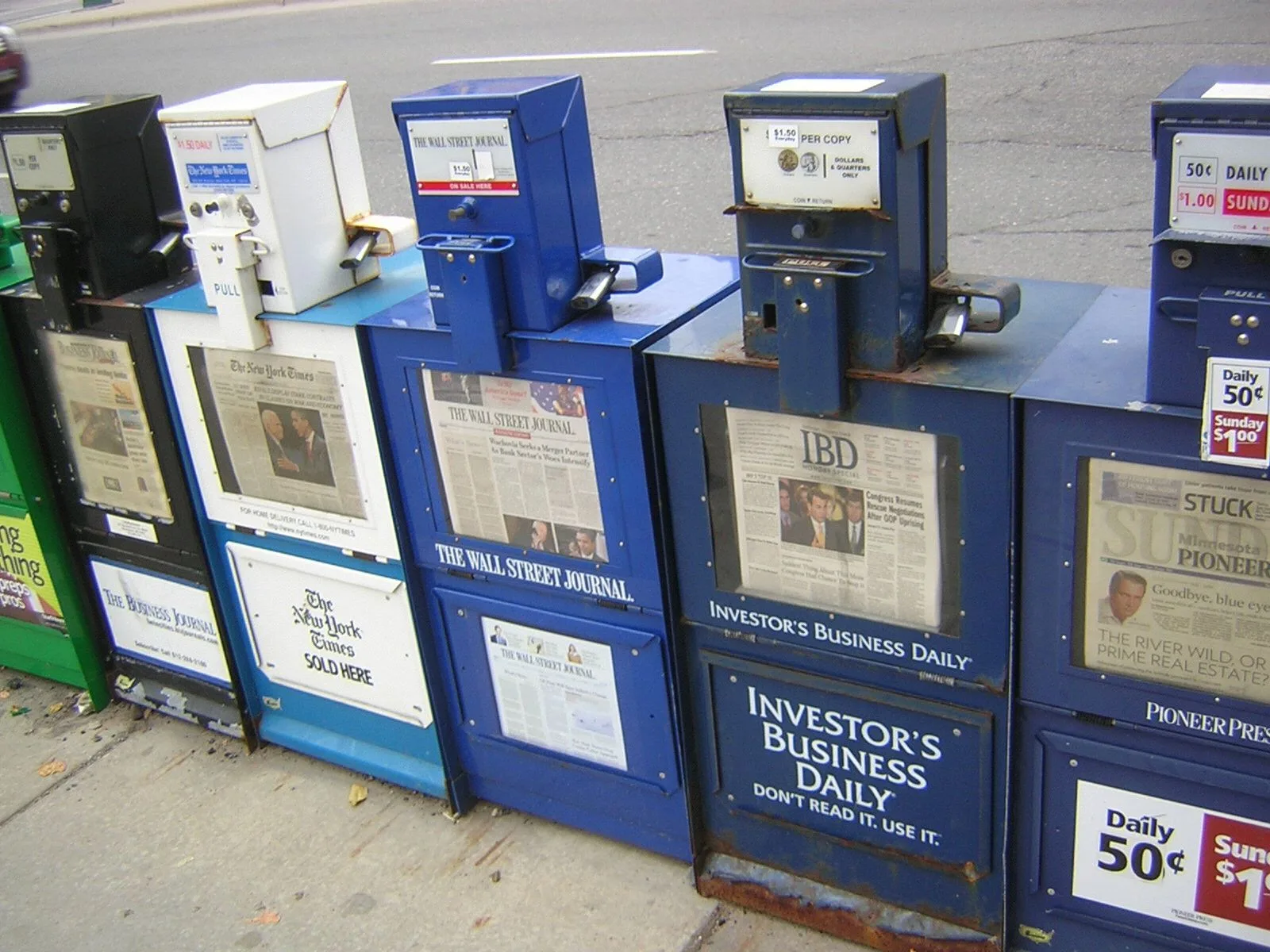 Newspaper vending boxes stand along a pavement on Washington Avenue in Minneapolis.