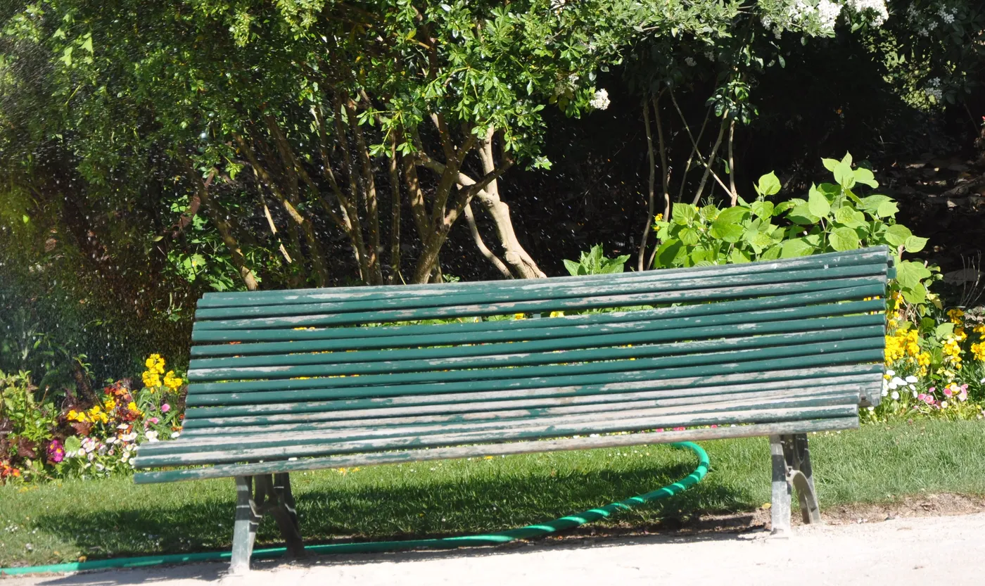 An empty green bench beside trees and flowers in a Paris garden.